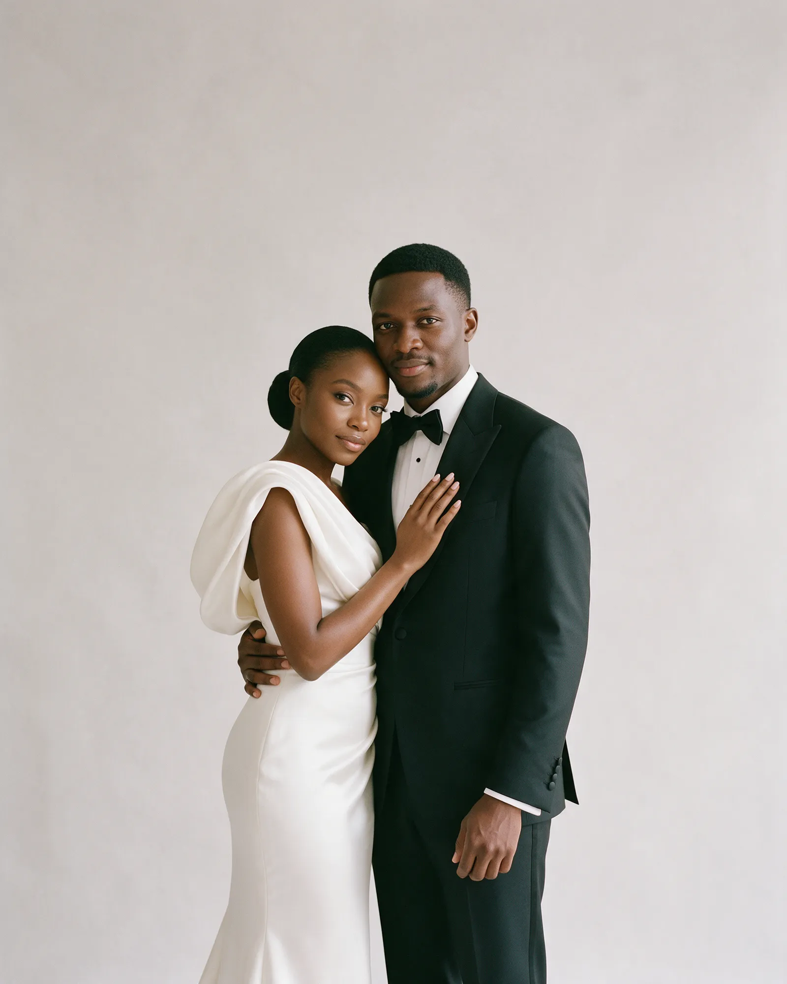 Mutinta in an ivory gown leaning into Kabwe in a black tuxedo